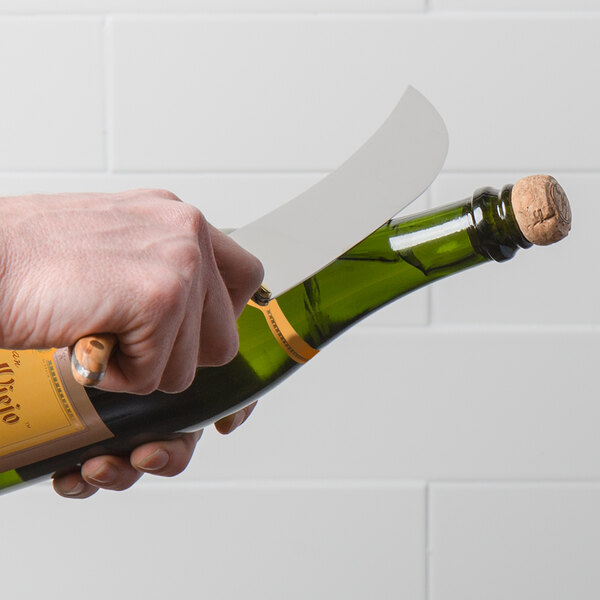 A person's hand holding a Laguiole champagne saber over a bottle of wine.