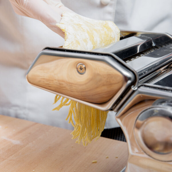 A gloved hand uses a Weston Roma Manual Pasta Machine to make noodles on a kitchen counter.