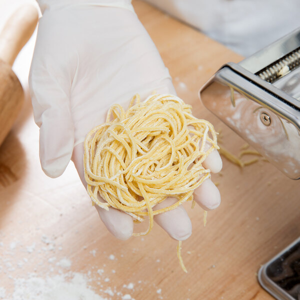 A person in a white glove using a Weston Roma Manual Pasta Machine to make noodles.
