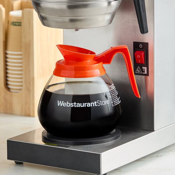 A glass coffee decanter with an orange handle labeled 'WebstaurantStore' placed on a coffee maker.