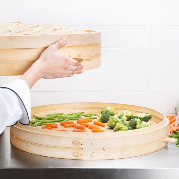 Town bamboo steamer set with a tray of steamed vegetables on a table.