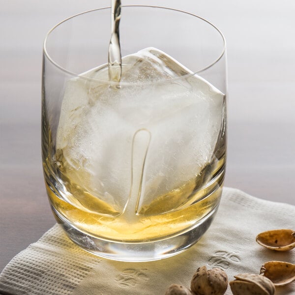 A glass of liquid with Franmara blue silicone ice cubes next to nuts.