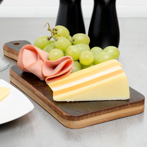 An American Metalcraft carbonized bamboo serving peel with cheese and grapes on it.