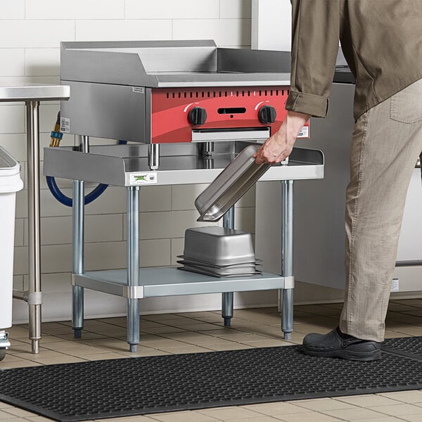 A man using a Regency stainless steel equipment stand near a stove.