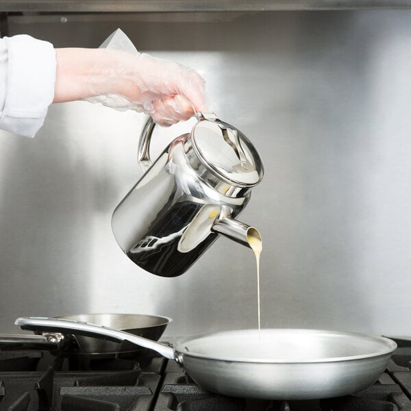 A person using a Vollrath stainless steel batter dispenser to pour liquid into a pan.