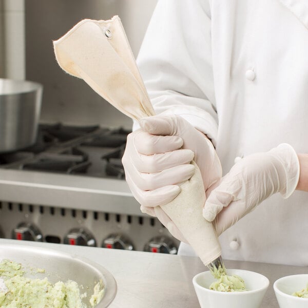 A chef in a white coat using an Ateco canvas pastry bag to put food into small cups.