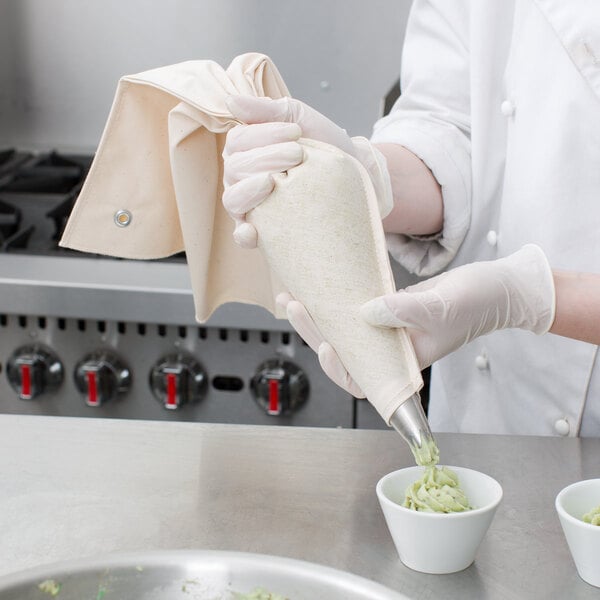 A person wearing gloves using an Ateco canvas pastry bag to pipe food.