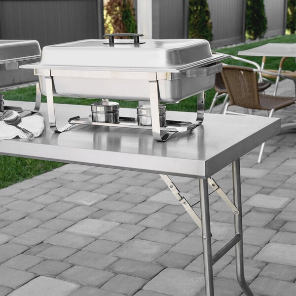 A Regency stainless steel folding work table set up with trays on top.