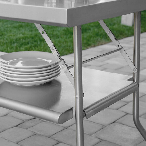 A Regency stainless steel folding work table with white plates on it.
