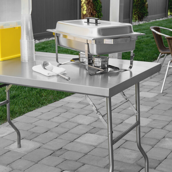 A Regency stainless steel folding work table with metal containers and a white towel on it.