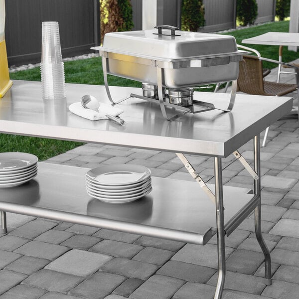 A Regency stainless steel folding work table with white plates and a metal container on it.