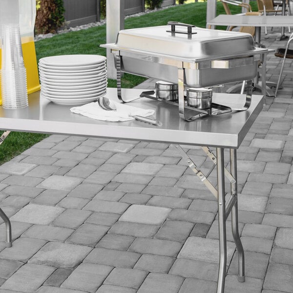 A Regency stainless steel folding work table with plates and bowls on it.