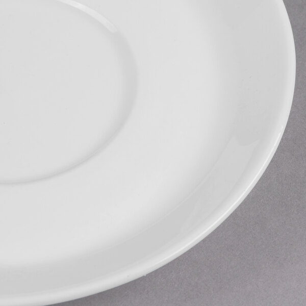 A close-up of a Libbey Ultra Bright White Porcelain Espresso Saucer on a gray surface.