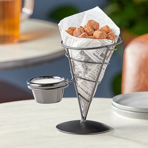 A Tablecraft wire cone basket with a ramekin holding brown food on a table with a newspaper.