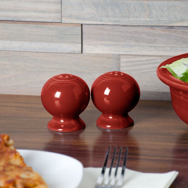 A white table set with red Fiesta salt and pepper shakers and a fork.