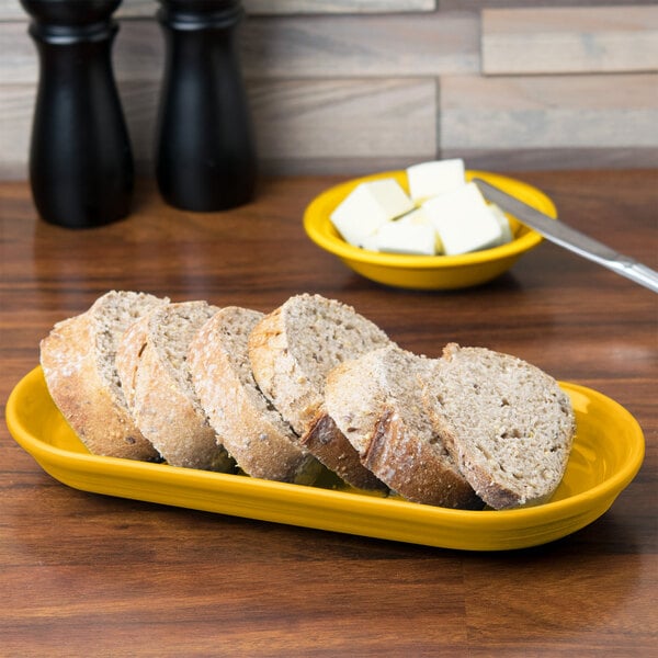 A yellow Fiesta oval china bread tray with sliced bread on it.