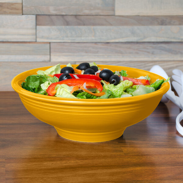 A Fiesta china pedestal serving bowl filled with salad and vegetables on a table.