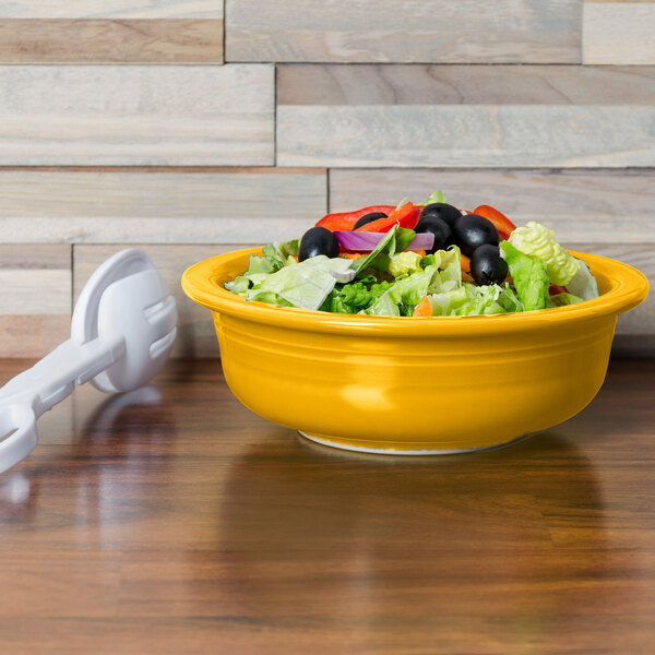 A Fiesta Daffodil china serving bowl filled with salad on a table.