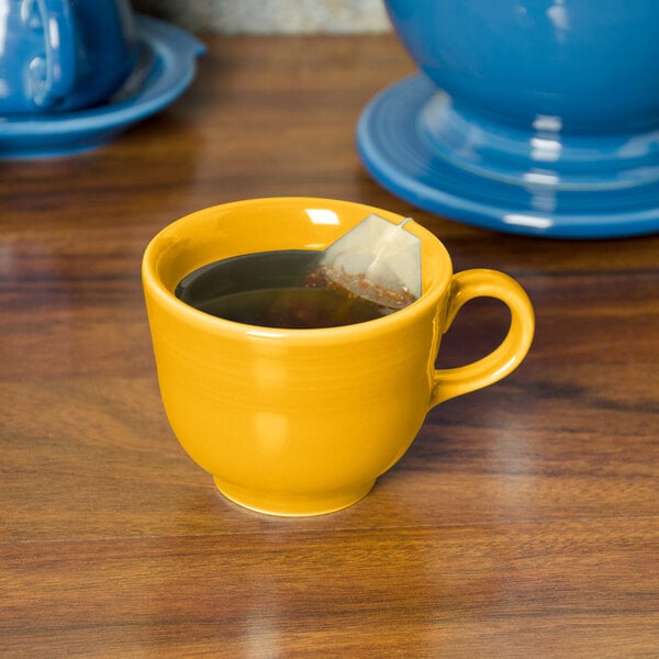 A yellow Fiesta china cup of tea with a tea bag in it on a table.