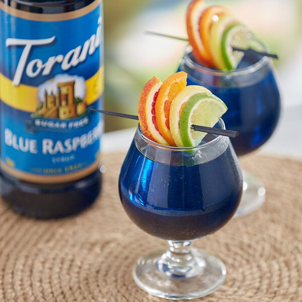 Two glasses of blue raspberry drinks with fruit slices on straws.