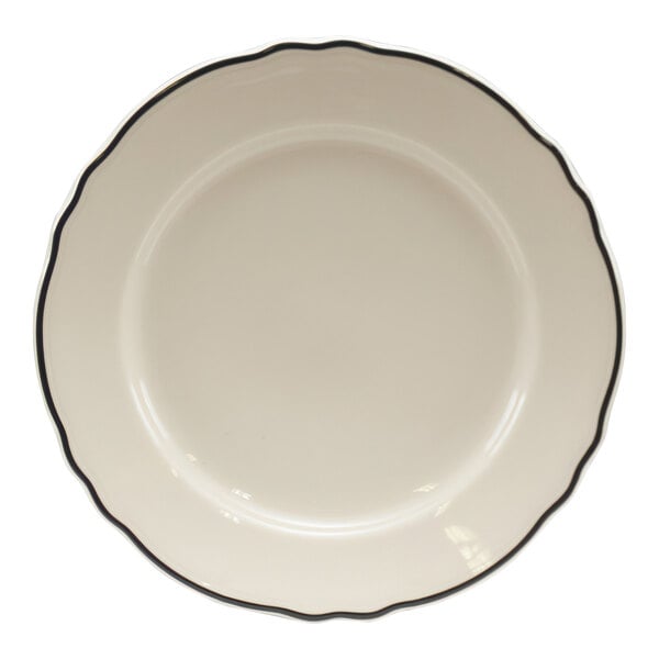 A white Homer Laughlin china bread and butter plate with a scalloped edge and black trim.