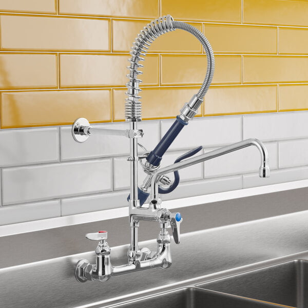 A commercial wall-mounted pre-rinse faucet with a flexible hose, spray valve, and an additional swivel spout installed above a stainless steel sink.