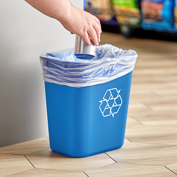 A hand putting a blue recycling can into a blue Lavex trash can.