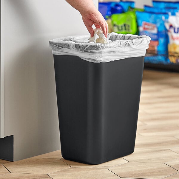 A person's hand lining a black Lavex trash can with a plastic bag.