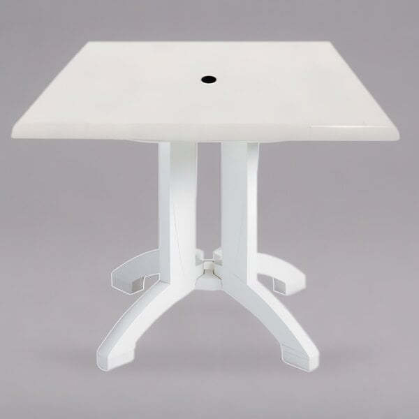 A white square table with legs and a black umbrella hole.