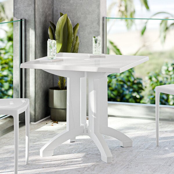 A white Grosfillex outdoor table with an umbrella pole on a patio.