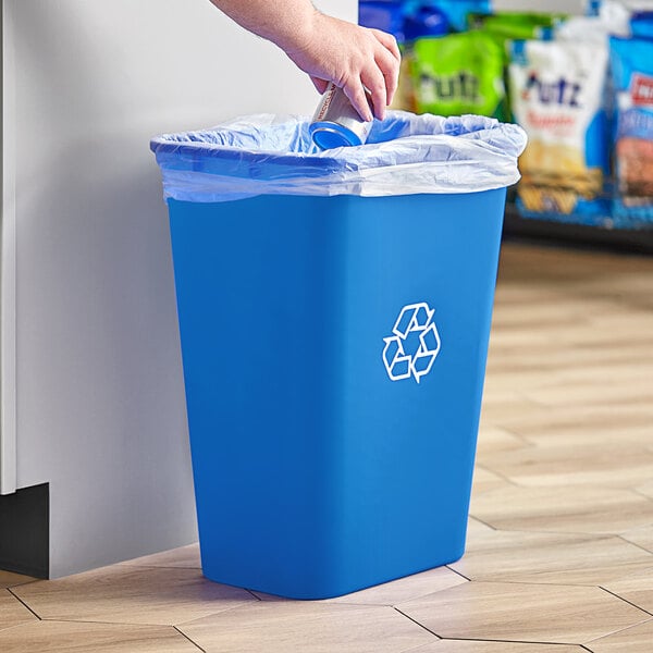 A hand putting a plastic can into a blue Lavex recycling bin.