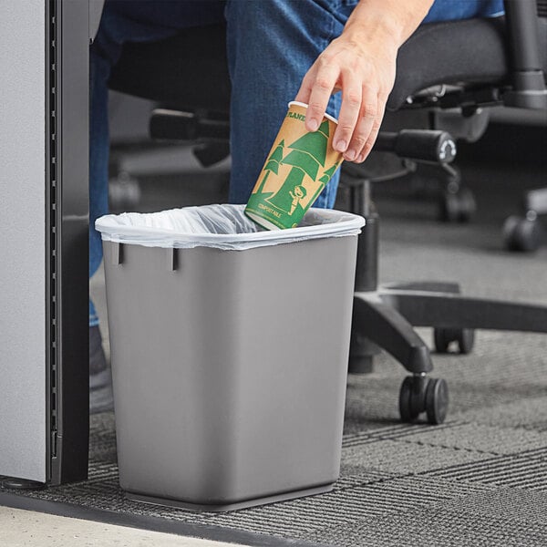 A hand putting a paper cup in a Lavex gray rectangular wastebasket