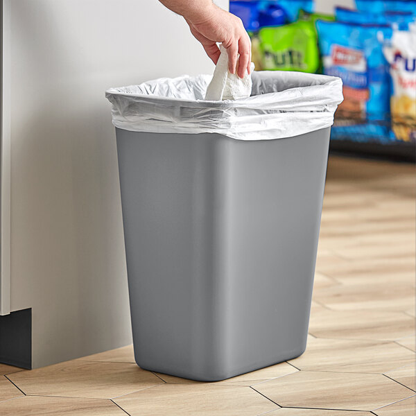 A hand putting a white paper towel in a grey Lavex trash can.