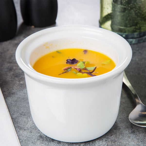 A white Tuxton china bowl filled with soup on a table with a spoon.