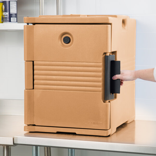 A hand opening a brown Cambro Ultra Pan Carrier box.