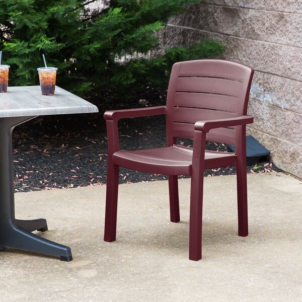 A Grosfillex Acadia Bordeaux resin armchair on an outdoor patio with a drink on the table.