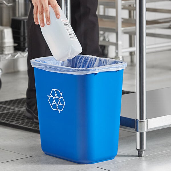 A person putting a plastic bottle into a blue recycling bin.