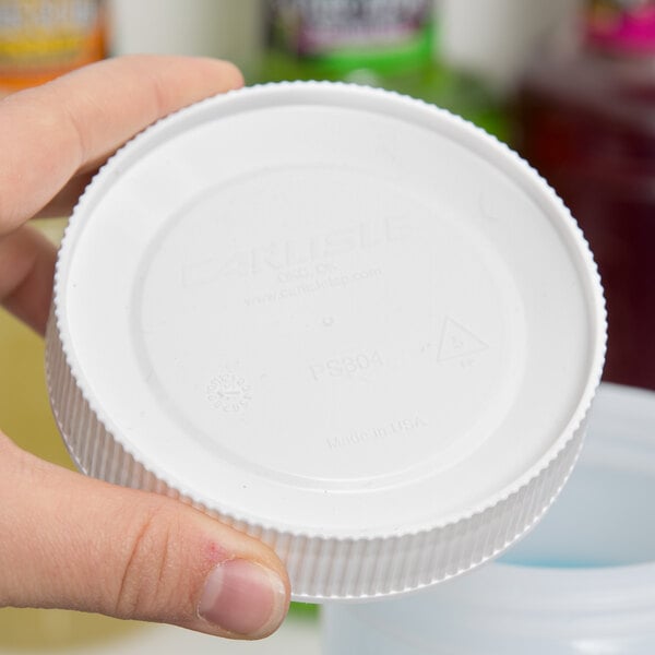 A hand holding a Carlisle white plastic lid with text.