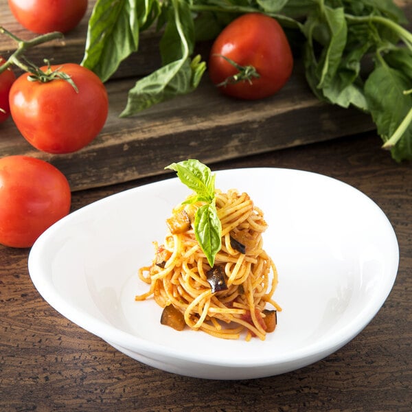 A Carlisle white melamine pasta plate with spaghetti, basil, and tomatoes.