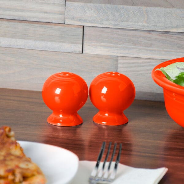 A bowl of salad, pizza, and Fiesta Poppy China salt and pepper shakers on a table.