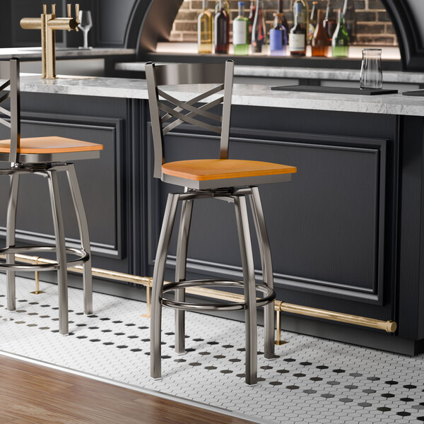 A metal bar stool with a cross back design and a cherry wood seat, featuring a swivel function.