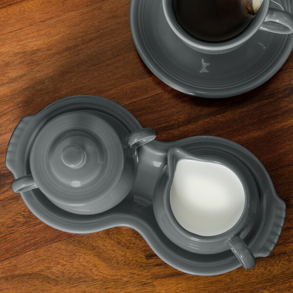 A Fiesta Slate china sugar and creamer tray with a cup of coffee and sugar on a table.