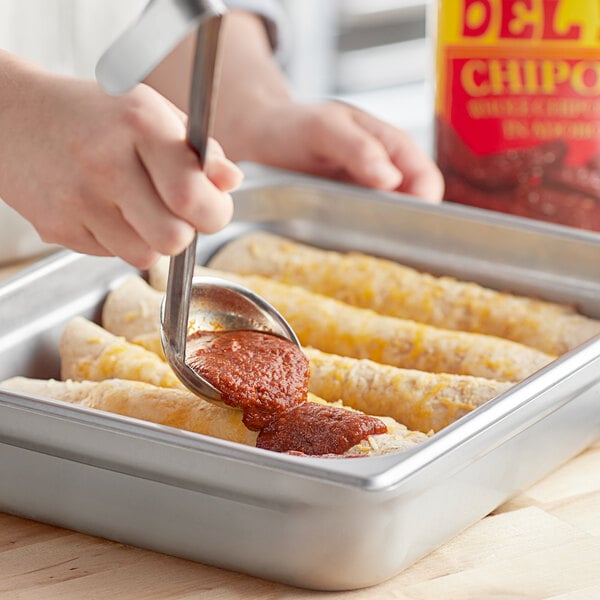 A person using tongs to pour adobo sauce onto burritos in a pan.