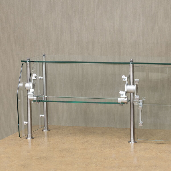 An Advance Tabco glass food shield with metal rods on a counter.