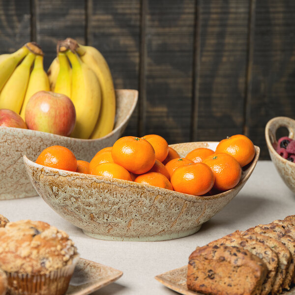 A table with 10 Strawberry Street Tiger Eye porcelain canoe bowls filled with fruit, including oranges, raspberries, apples, and bananas.