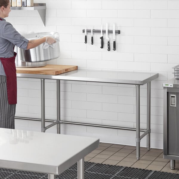 A woman standing in a kitchen with a Regency stainless steel work table.