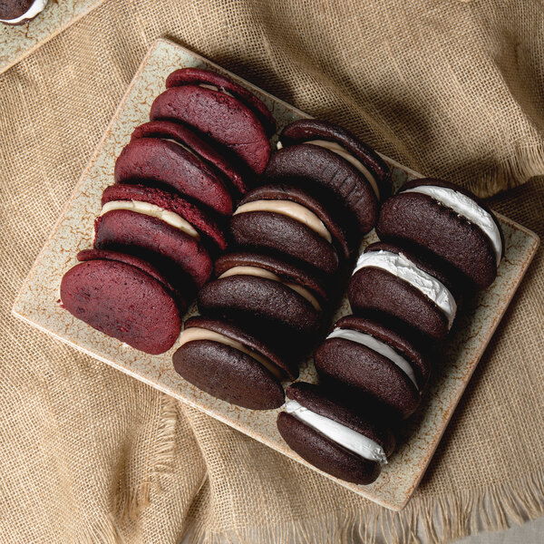 A rectangular porcelain platter with chocolate and red velvet sandwich cookies on it.