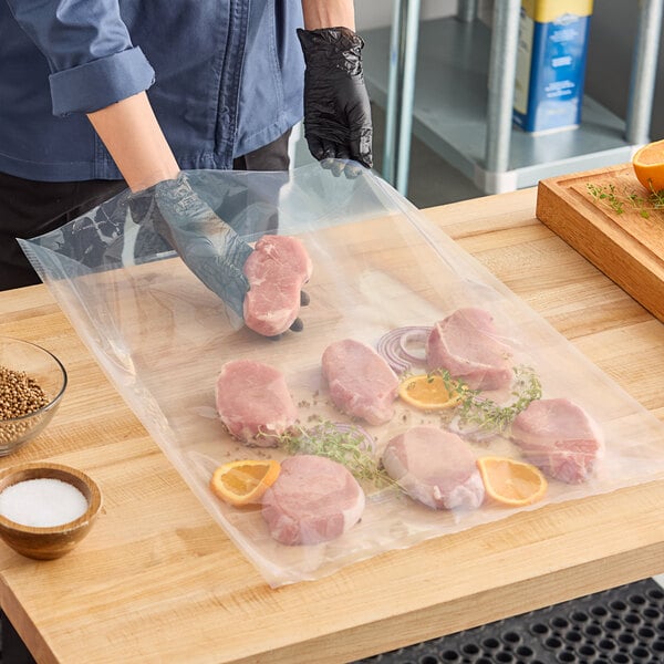 A large clear vacuum packaging pouch containing several pieces of raw meat with herbs and orange slices on a wooden countertop.