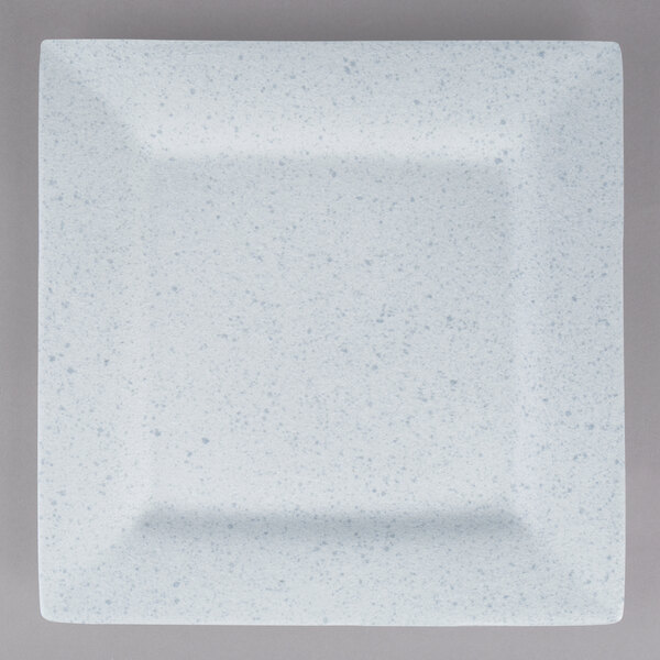 A white square porcelain charger plate with blue speckled specks.