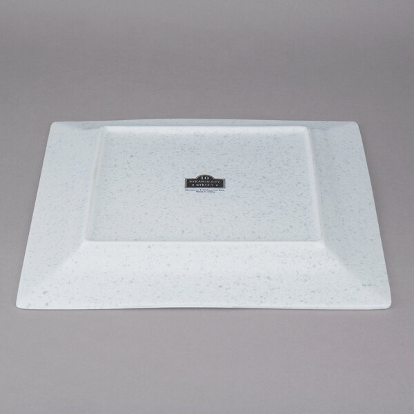A white square porcelain charger plate with a black label on a counter.
